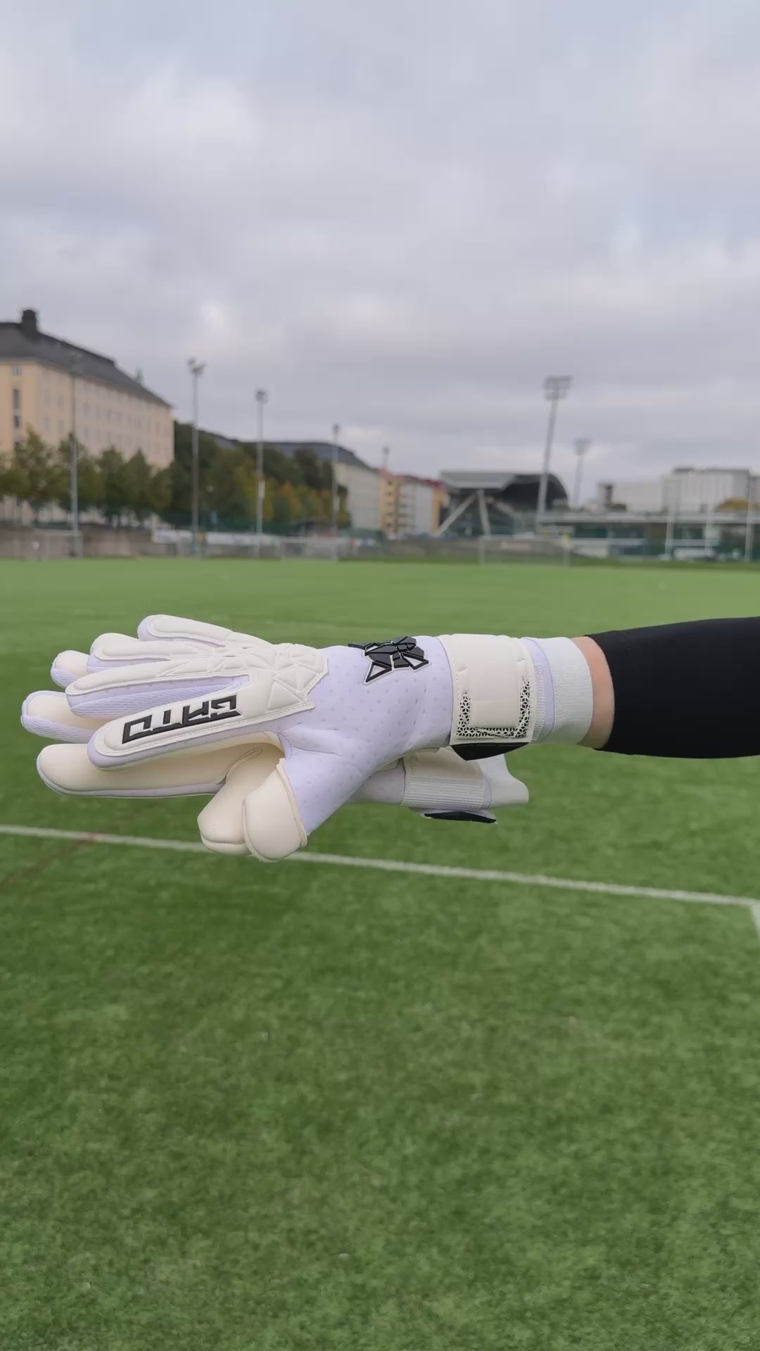 Goalkeeper putting on white GATO Classic Match goalkeeper gloves on an artificial turf pitch